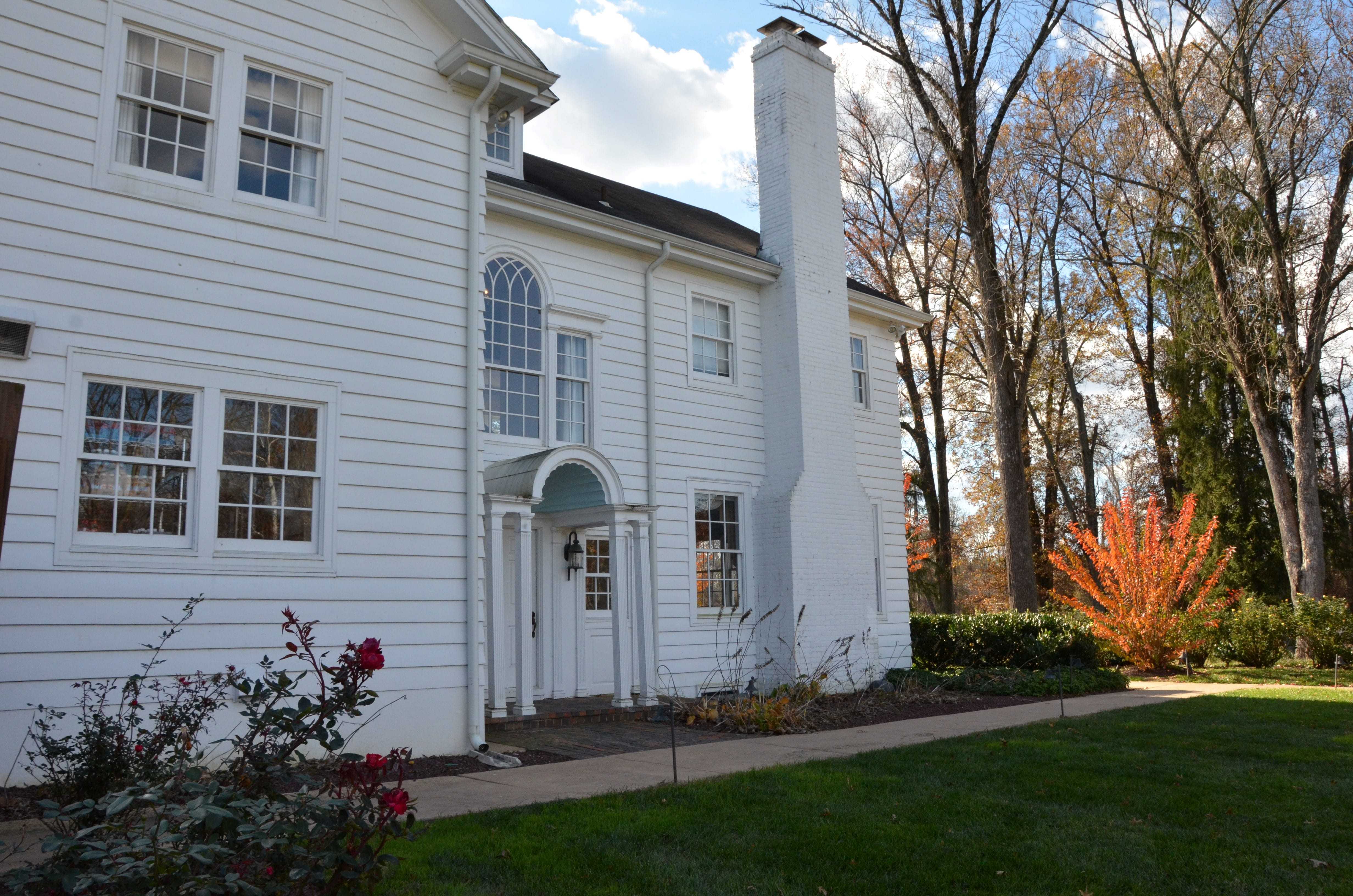 A facade of the white manor with tall, bare trees to the right of it.